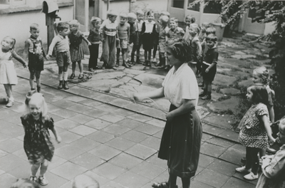 876950 Afbeelding van een groep kleuters die toekijkt bij het touwtjespringen op de binnenplaats van het Klooster ...